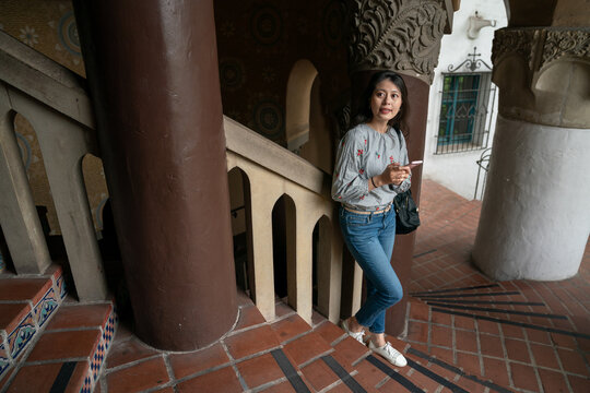 full length of amazed asian Korean lady tourist leaning against stair railing and looking up at beautiful interior design of santa Barbara county courthouse in California usa