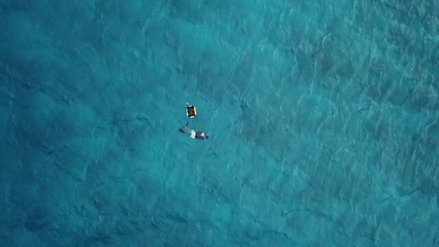 Drone post view of asian man floating in the Indian ocean and searching seashells.Maldives