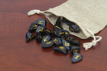 Black stone runes with burlap sack on wooden table.	