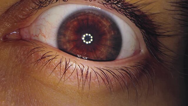 A close-up of eye in which light shines from medical device studying the iris and pupil. The topic of diagnostics in ophthalmology and the health of the eyeball. A man looks at the camera in close-up.