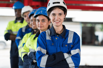 Group of male and female factory workers standing together with crossed arms and smiling in industry factory, wearing safety uniform and helmet. Factory workers working in factory