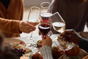 Closeup of group of people toasting with wine glasses at festive dinner table celebrating Thanksgiving together, copy space - Powered by Adobe