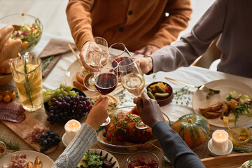 Diverse group of people toasting with wine glasses at festive dinner table celebrating Thanksgiving...