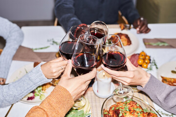 Close up of group of friends toasting with red wine glasses at dinner table, shot with flash