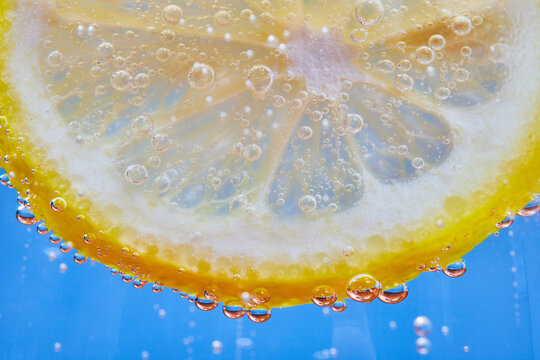 Macro of bubbles on curved edge of yellow lemon slice with blue background