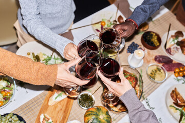High angle closeup of friends toasting with red wine glasses while celebrating at dinner table, shot with flash