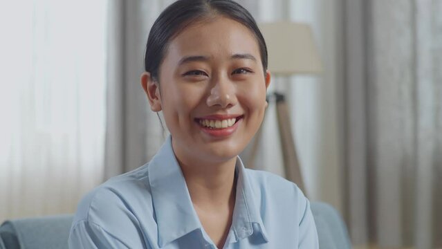 Close Up Of Asian Woman Smiling To Camera While Sitting On Sofa In The Living Room 
