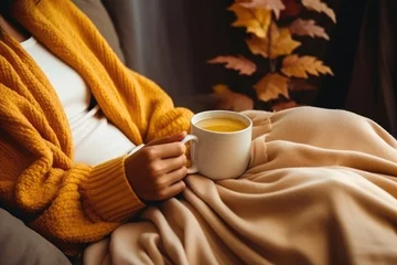 Rolgordijnen woman drink tee on a couch with cozy blanket in autumn © krissikunterbunt
