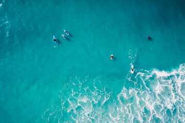 Surfers rowing on surfboards in transparent turquoise ocean waiting wave. Aerial view