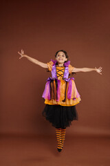 happy girl in colorful Halloween costume looking at camera and jumping on brown background, levitate