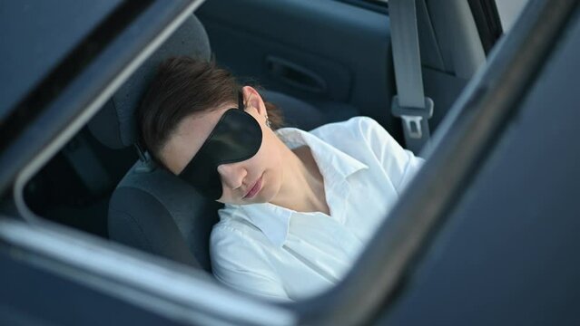 View through the sunroof of a young woman sleeping in the driver's seat with a sleep mask over her eyes