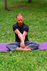 Naklejka na ściany i meble handsome bearded man meditating in the park practicing yoga doing stretching and exercises for different muscle groups