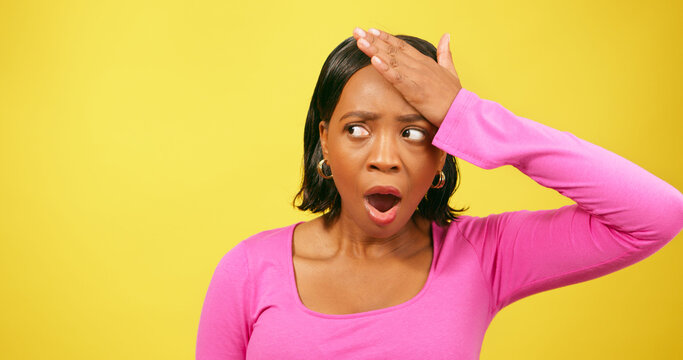 Shocked and upset young woman puts hands to head, yellow studio background
