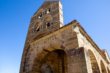 Iglesia románica con espadaña con campanas sobre un cielo azul.