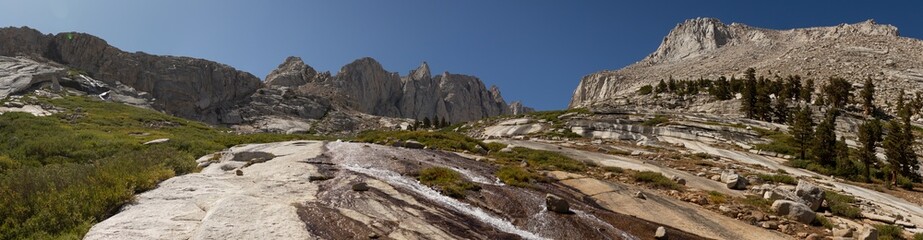 Panorama shot of colorful granite rocks and water over them. Blue sky and tops of Mount Whitney, usa