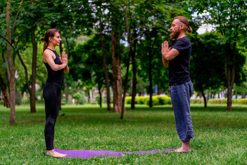 Obraz premium couple practicing yoga outdoors in a city park doing meditation exercises with namaste gestures people focus on mental and spiritual health