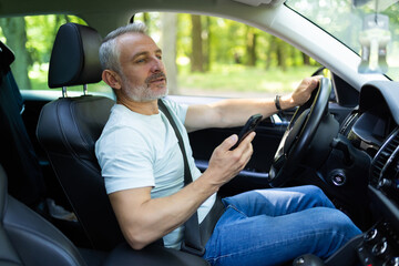 Middle aged man using a smart phone while driving a car in the street