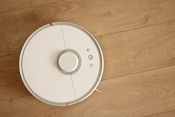 Top view of white wireless autonomous robotic vacuum cleaner on wooden floor. Smart cleaning technology. Self-propelled cleaning robot. Floor cleaning system. Household remote control appliances.