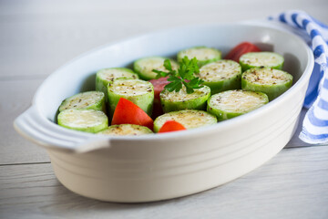 Raw zucchini with tomatoes prepared for baking in a ceramic form.