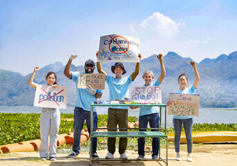 group of volunteers holding environmental campaign signs standing by the river, dead fish and rubbish on table. concept of environmental conservation, save planet, earth day in April