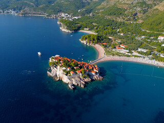Aerial view of Sveti Stefan island and shore in a beautiful summer day, Montenegro from flying drone. Panoramic above view of Saint Stephen luxury resort. Tourism and leisure concept. Aero photography - obrazy, fototapety, plakaty