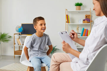 Child boy sitting on chair on check up session consultation with woman psychologist in elementary...