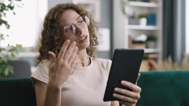 Nice curly having video call from home spends time conversating with work colleague, sitting on couch in brightly lit room