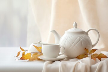 Cozy autumn still life with white ceramic teapot kettle, cup and fall leaves. Vintage white tea kettle with hot steam, cup and plants on white background