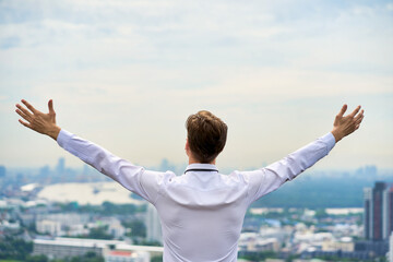 Businessman back view cityscape background. Businessman spreading arms wide open.