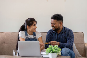 Happy couple using credit card to make online purchases on laptop in living room.