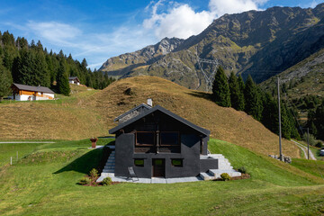Fototapeta na wymiar A very unusual Swiss mountain chalet because it is black and made of wood. Around a beautiful green summer meadow