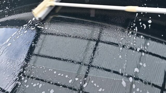 Someone using a glass wiper for cleaning a car windshield. It&rsquo;s important to keep a car&rsquo;s front window clear of any visual obstruction for safe driving and to keep the car presentable.