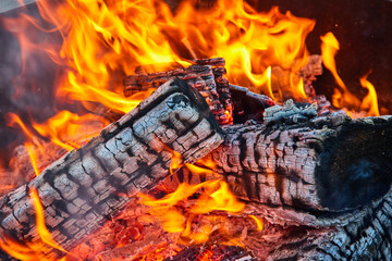 Orange and yellow flames surrounding three charred black logs with white ashes in circular pit