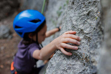 rock climber's hand close-up. child rock climber in a blue protective helmet overcomes the route in...