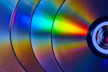 Abstract stack of four silvery CDs with reflective rainbow bursts of light on surface