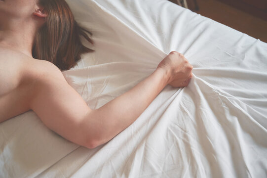 Healthy sex life concept. Unrecognizable woman grabs the sheet of the bed while having an orgasm.