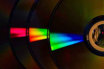 Abstract stack of four dark silvery CDs with reflective rainbow bursts of light on surface