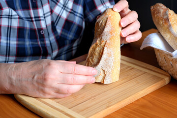 Hands of an elderly woman holding sliced white wheat bread baguette