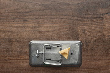 Piece of cheese in metal mousetrap concept. Top view of the rat trap on wooden background with copy space.