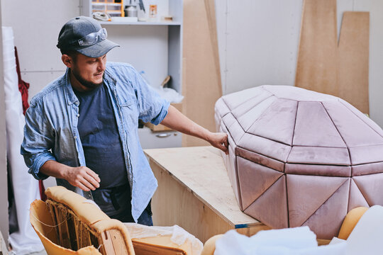 Carpenter works makes pink velvet coffin in carpentry workshop. Man doing furniture professionally.