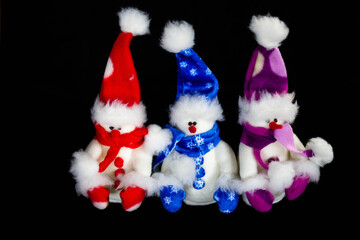 Three handmade toy snowmen with hats and scarves on a black background. Made of felt, scarf, black button, close up. Decor. Christmas and New Year concept