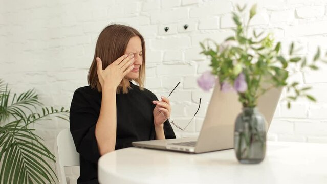 Tired young woman worker student take short pause in online work remove glasses, rubs eyes and massage nose bridge with closed eyes. Girl employee overworked by pc feel fatigue suffer from eye strain.