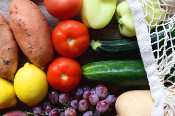 Reusable mesh bag with seasonal fruit and vegetable on wooden background. Late summer or early autumn. Top view.