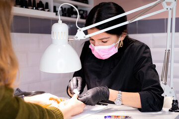 manicurist working at the table wearing black gloves and a mask. Nails beauty salon. Profession manicurist