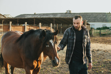 A young farmer works in a paddock with horses. A young man takes care of horses on a farm.