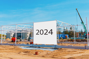 Construction site with crane and numbers 2024 new year billboard in foreground.Blue sky,summer hot...