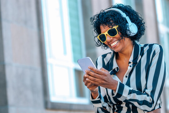 woman with headphones and mobile phone smiling with yellow sunglasses