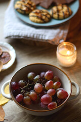 Cup of tea or coffee, plate with desserts, dried oranges, bowl of grapes, scented candles, vintage books, pumpkins and autumn leaves on the table. Autumnal hygge. Selective focus.