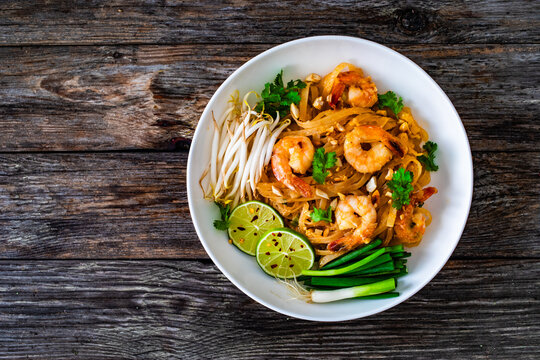 Pad Thai with prawns and rice noodles in peanut and tamarind sauce on wooden table

