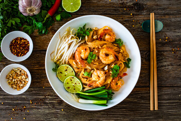 Pad Thai with prawns and rice noodles in peanut and tamarind sauce on wooden table
